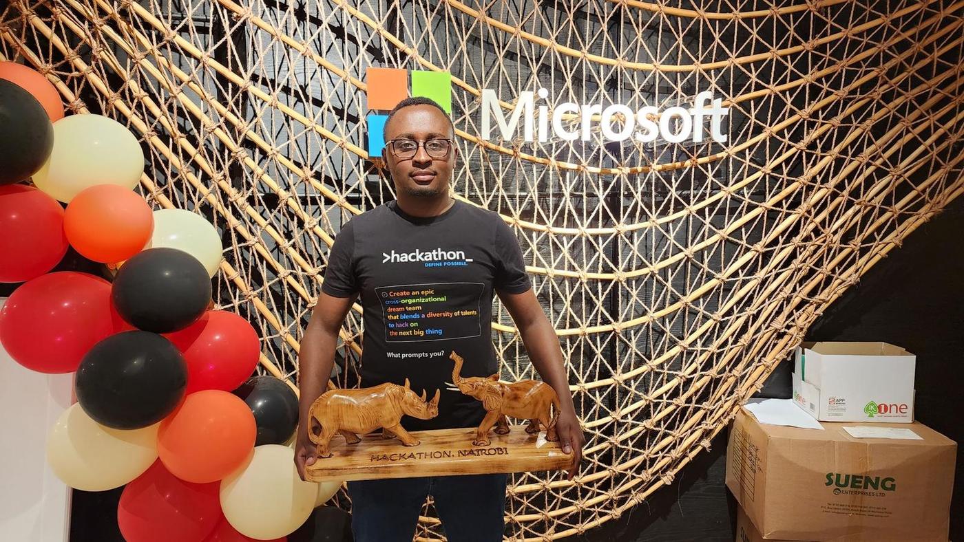 Holding the carved Hackathon Nairobi trophy in front of the Microsoft logo