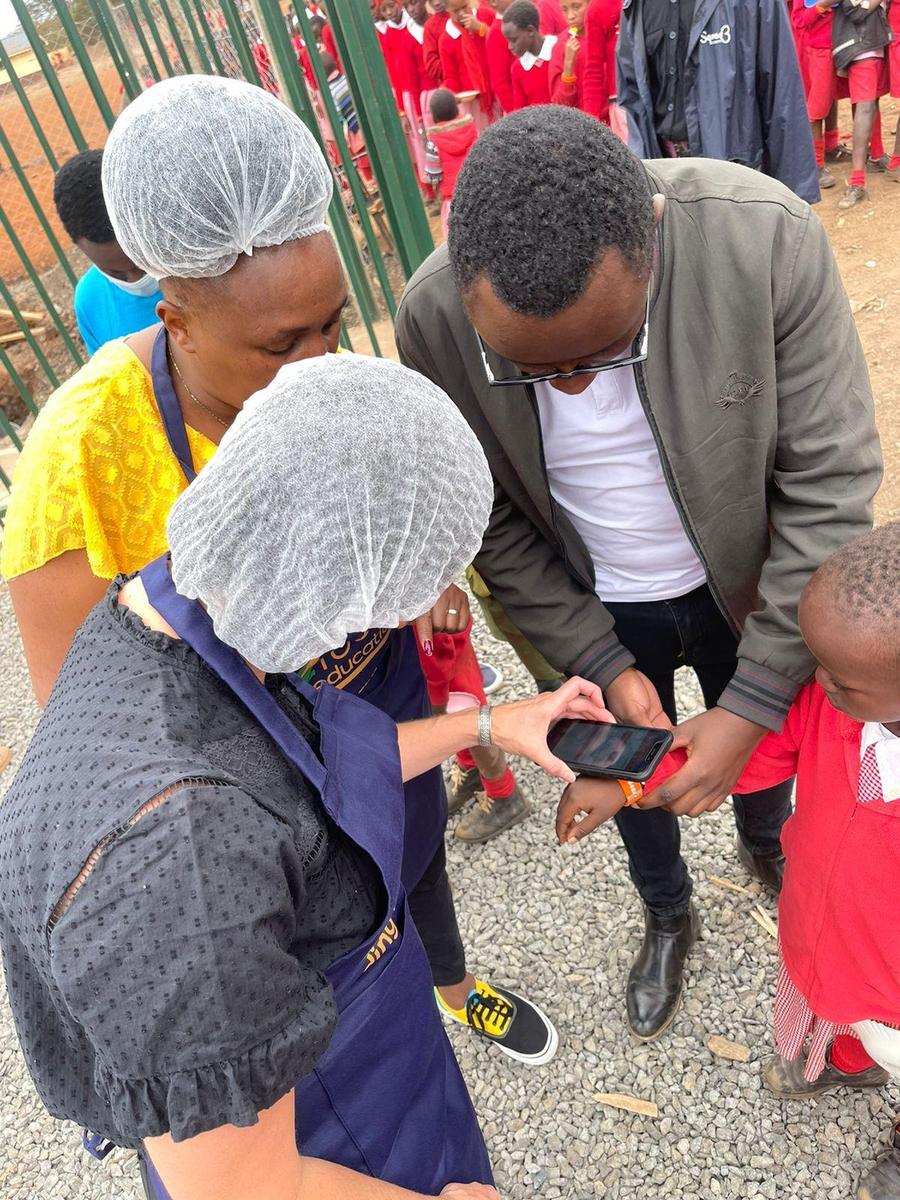 A child taps an orange Tap2Eat wristband against a phone at a school food station
